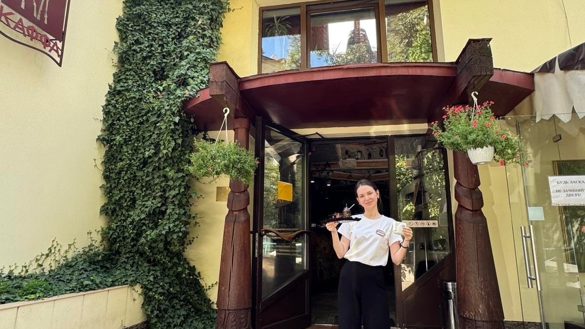 Службовиця в ресторані з подачею страв на підносі, популярний затишний заклад у Києві, оточений зеленню і квітами, що створює атмосферу гостинності та комфорту для відвідувачів.