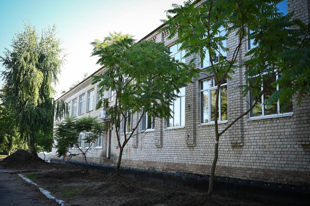 Фасад цегляної будівлі з великими вікнами та молодими деревами перед нею