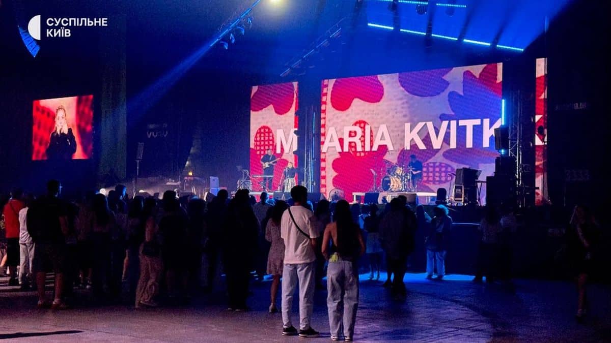 Виступ на відкритій сцені з великим екраном, де показано ім’я МАРІЯ КВІТКИ, та аудиторія збирається на концерт у Києві.