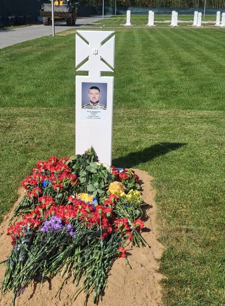 Могила українського військового з білою табличкою, портретом загиблого та великою кількістю квітів
