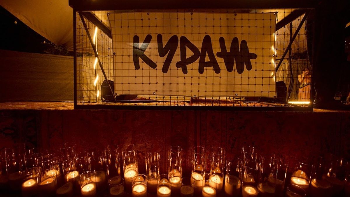 Темний стенд із написом «Кураж» за сіткою, під яким горить багато свічок у скляних свічниках