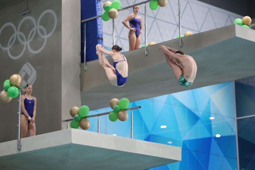 Двоє спортсменів одночасно виконують синхронний стрибок у воду з вишки
