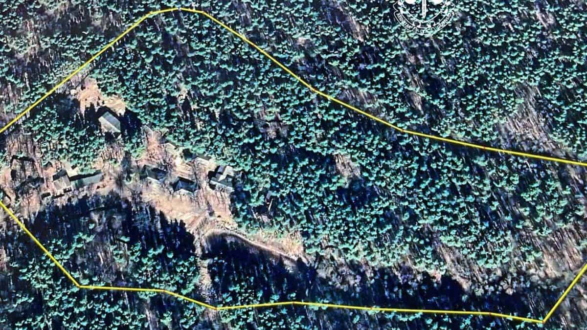 Високий аерофотознімок густого лісу з невеликими хатами, обмеженого жовтою лінією, в центрі зображення.