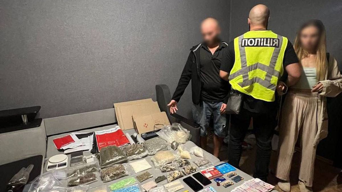 Поліцейський у жилеті поруч із затриманим чоловіком і жінкою, поруч вилучені наркотики, гроші та банківські картки