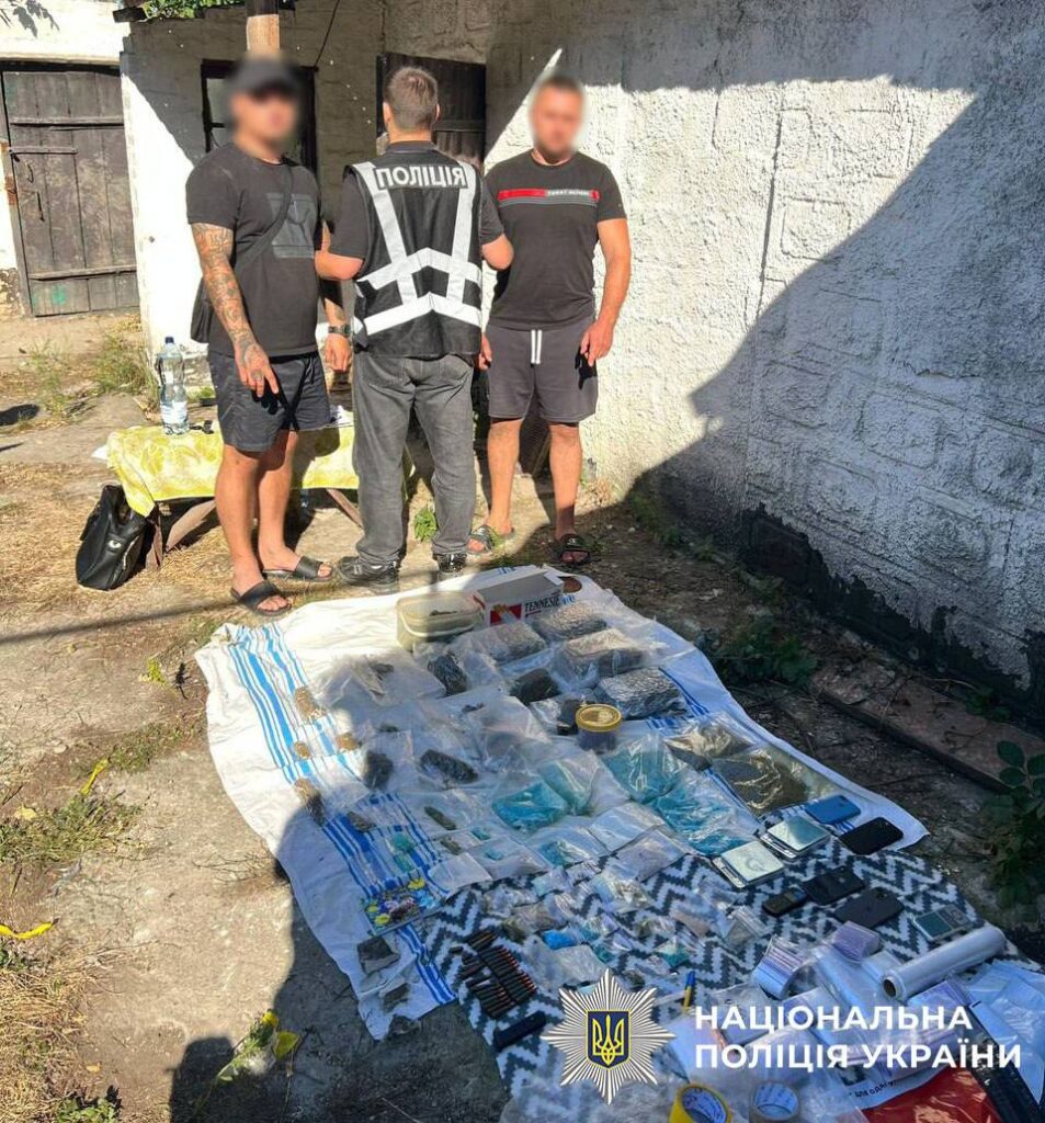 Двоє чоловіків біля поліції, на землі розкладені пакети з наркотиками, патрони та ваги