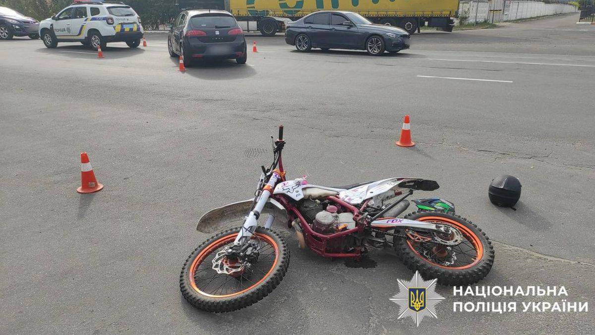 На асфальті лежить пошкоджений мотоцикл із яскраво-помаранчевими дисками, поряд чорний шолом