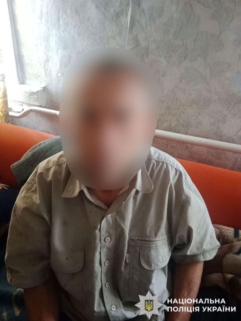 Чоловік у сірій сорочці сидить у кімнаті на дивані, його обличчя навмисно розмите