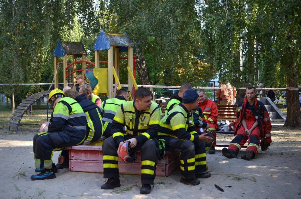 Допомагаючі рятувальники сидять у парку, після евакуації дітей з пошкодженої ігрової зони у Києві через можливо обстріл або вибух.