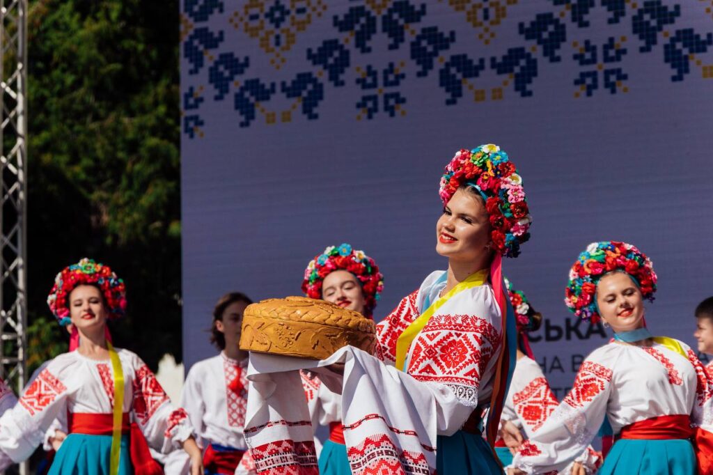 Українська дівчина у традиційному вбранні із вінком із квітів, тримає хліб та сіль, святкова культурна подія, українські народні танці, фестиваль, Київ, Україна.