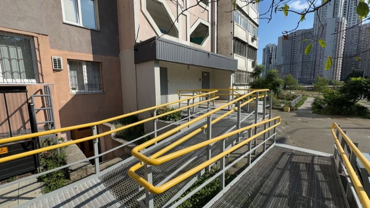 Пандус із жовтими поручнями біля входу до багатоповерхового будинку