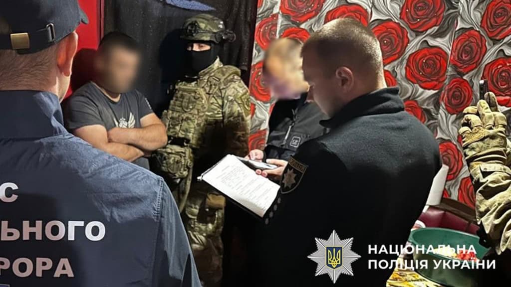 Викрали 1 млн у звільнених з полону військових: поліція затримала шахраїв 5 людей стоять в кімнаті будинку, двоє з них працівники поліції з документами