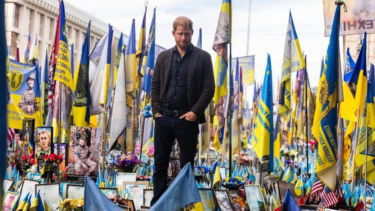 Чоловік у темному одязі стоїть серед сотень українських прапорів і фотографій загиблих військових на меморіалі, присвяченому захисникам України