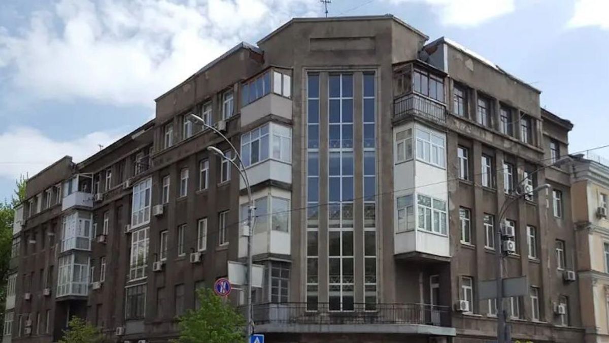 Сіра будівля на вулиці Інститутській у Києві з великими вертикальними вікнами посередині та заскленими балконами з боків