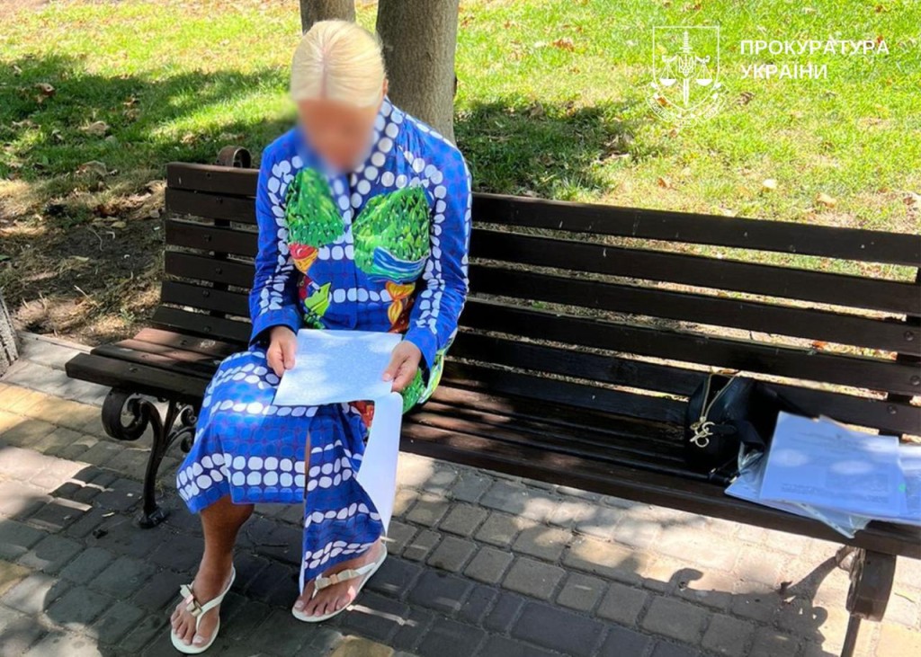 Жінка з розмитим обличчям у яскравій синій сукні сидить на лавці в парку та читає документи