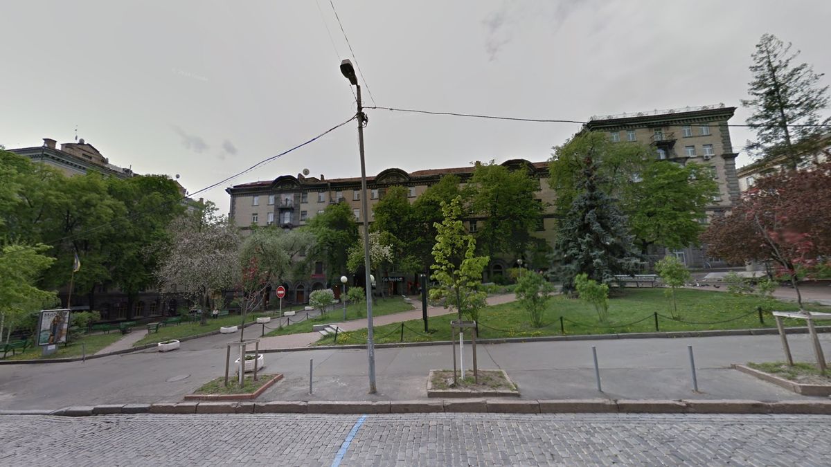 Зелені дерева і лавки у парку на тлі історичної будівлі в Києві в сонячний день.