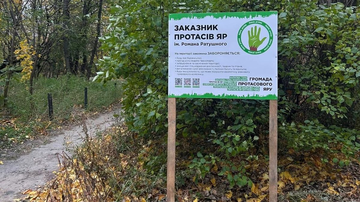 Інформаційний стенд заказника «Протасів Яр» імені Романа Ратушного серед дерев уздовж лісової стежки