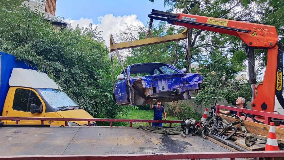 Кран піднімає синій пошкоджений кузов автомобіля й вантажить його на платформу евакуатора