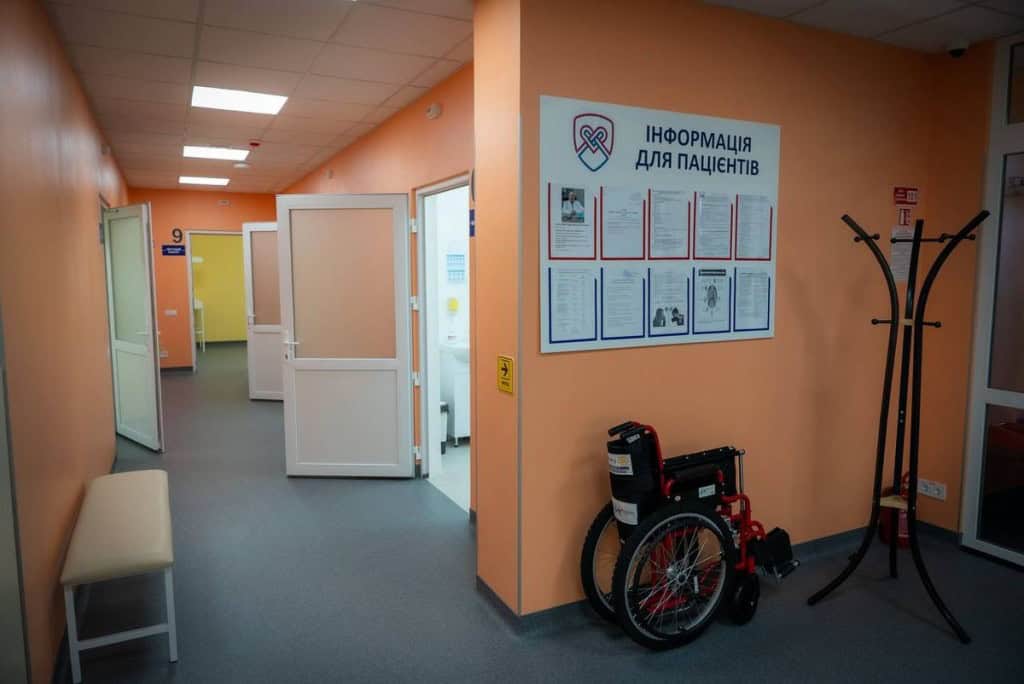 Бориспільщина: у Рогозові відкрили нову амбулаторію сімейної медицини Коридор медичного закладу з відкритими дверима кабінетів, стендом з інформацією для пацієнтів і складним кріслом колісним