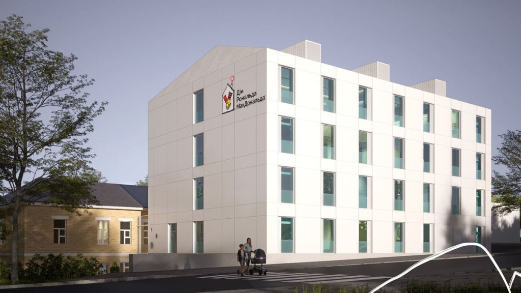 Білий сучасний будинок з логотипом «Дім Рональда МакДональда» на фасаді, поруч людина з дитиною та візочком