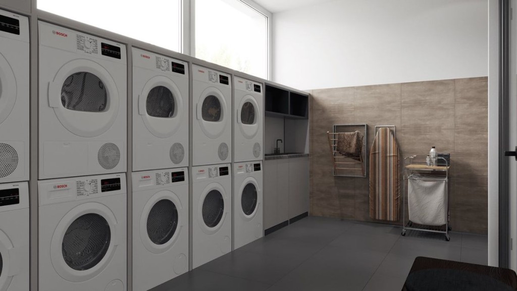Пральня з кількома рядами пральних і сушильних машин, поруч прасувальна дошка та кошик для білизни