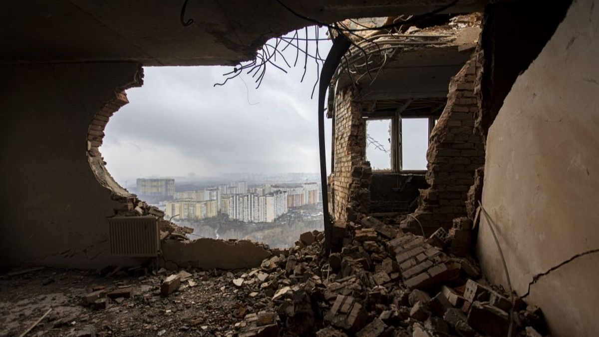 Зруйнований будинок у Києві з відкритим вікном, що відкриває панорамний вид на міські жовто-блакитні багатоповерхівки, зруйнований під час бойових дій, руйнування та обламки цегли.