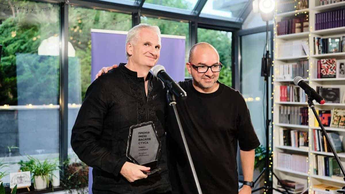 Двоє чоловіків стоять біля мікрофона у світлому приміщенні з книжковими полицями