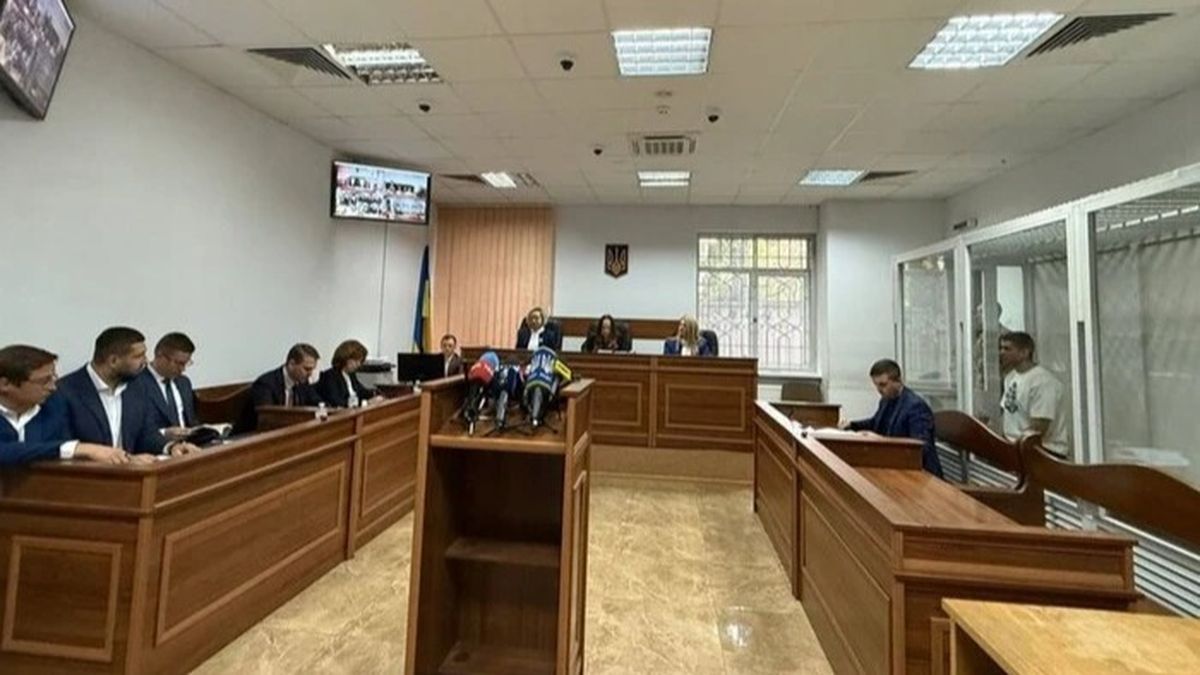 Засідання в українському суді: за довгими дерев’яними столами сидять адвокати й прокурори, попереду три судді
