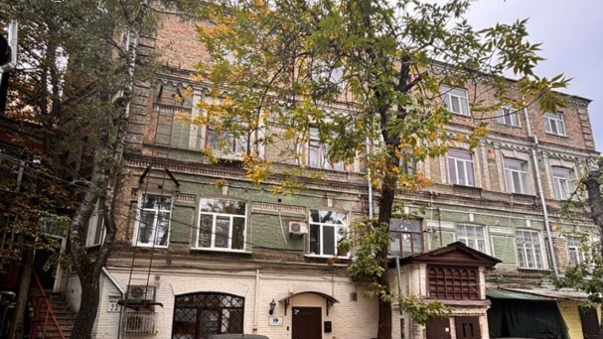 Будівля у центрі Києва має кілька поверхів із характерною старою цегляною архітектурою та зеленим фасадом