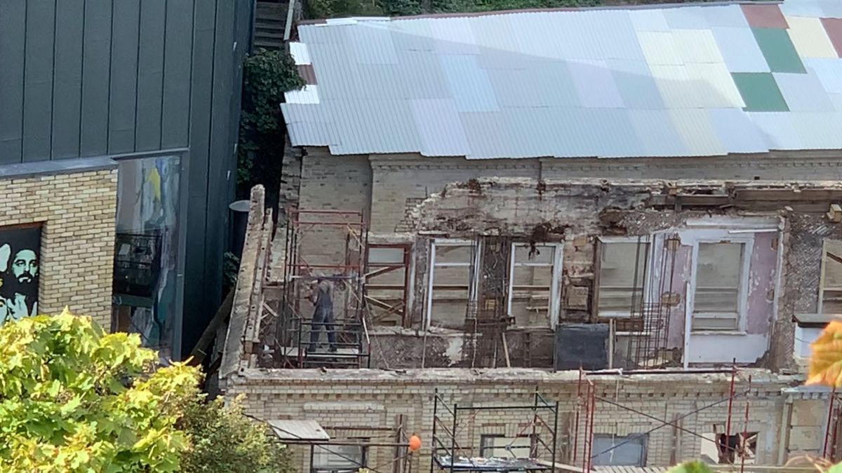 Будівля з цегли у стані реконструкції: частина фасаду розібрана, видно старі вікна й пошкоджені стіни