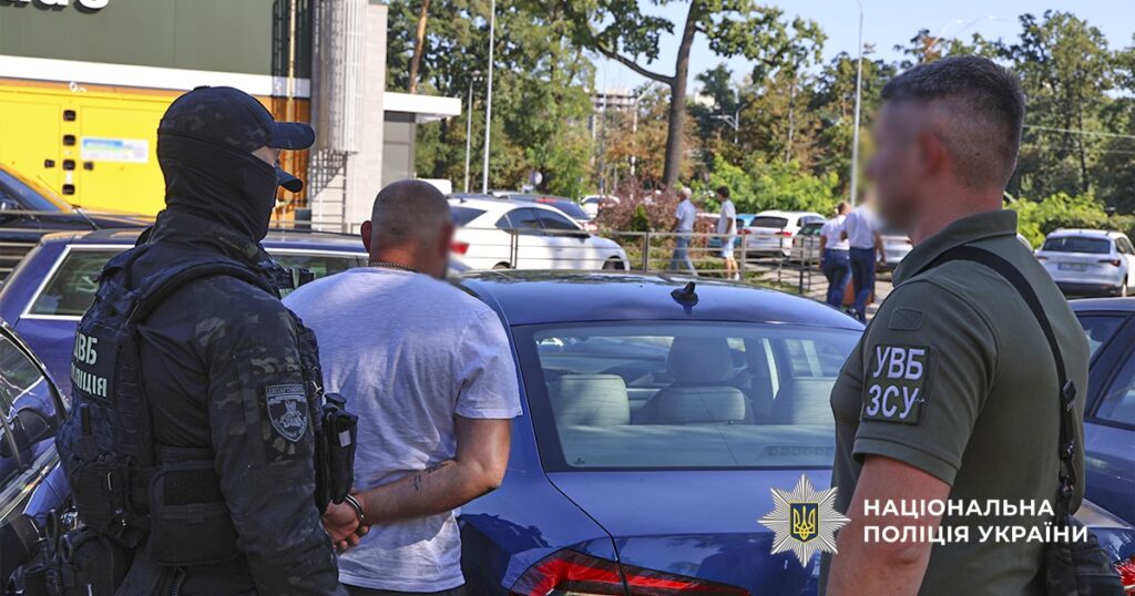 Повішений чоловік у руках поліції біля авто на вулиці Києва під час спецоперації. На зображенні присутні співробітники правоохоронних органів під час затримання.
