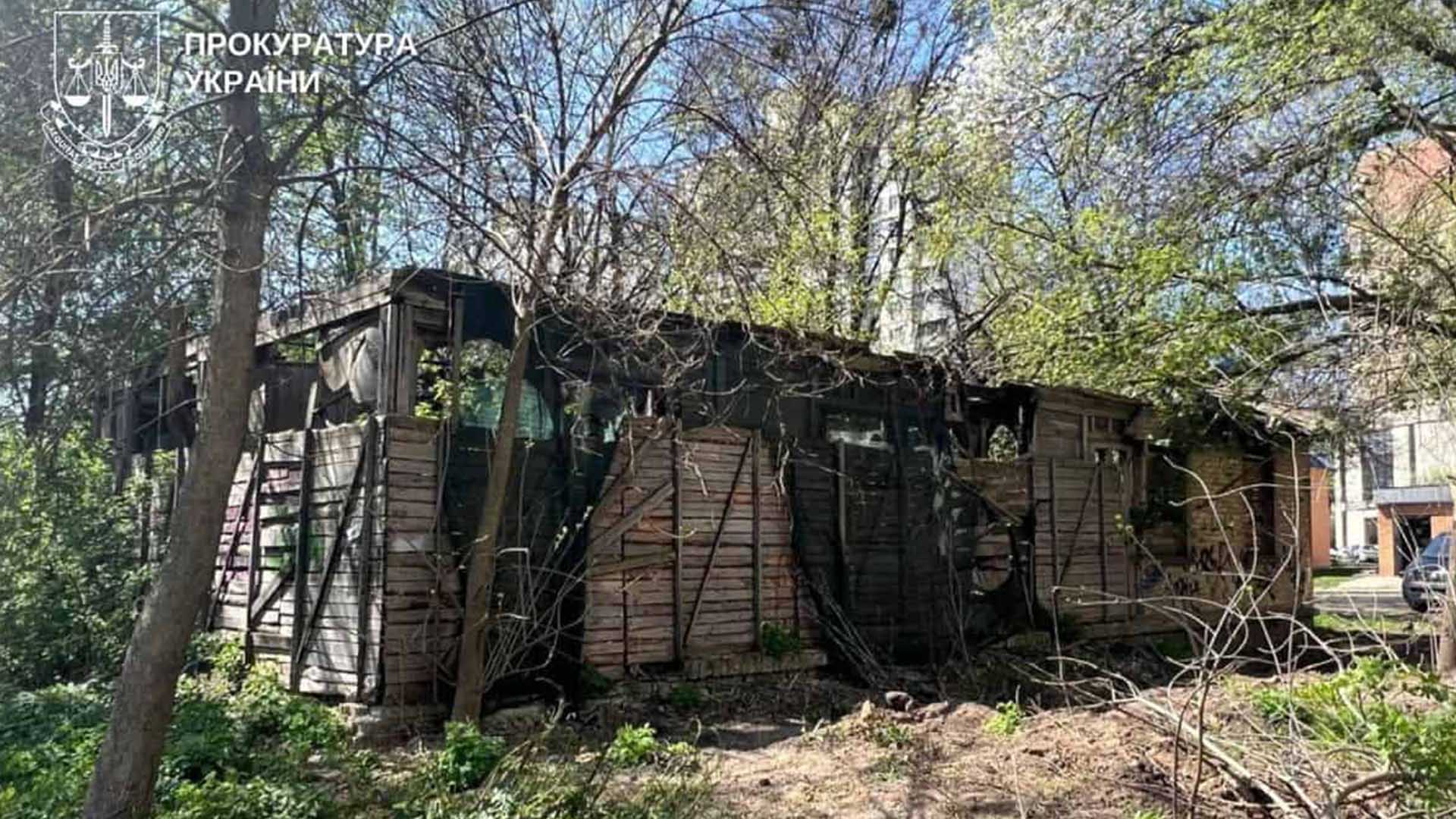 Занедбана дерев’яна будівля з пошкодженими стінами та дахом, зарослий деревами й кущами