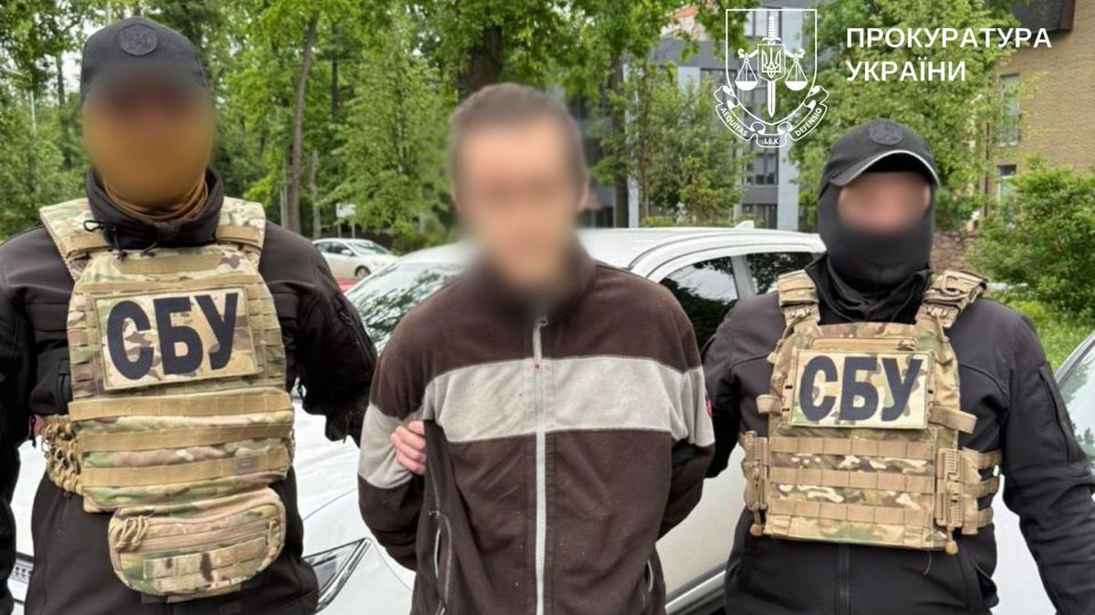 Двоє співробітників СБУ у камуфляжних бронежилетах із написом «СБУ» затримують чоловіка у темній куртці з білою смугою, ведучи його за руки