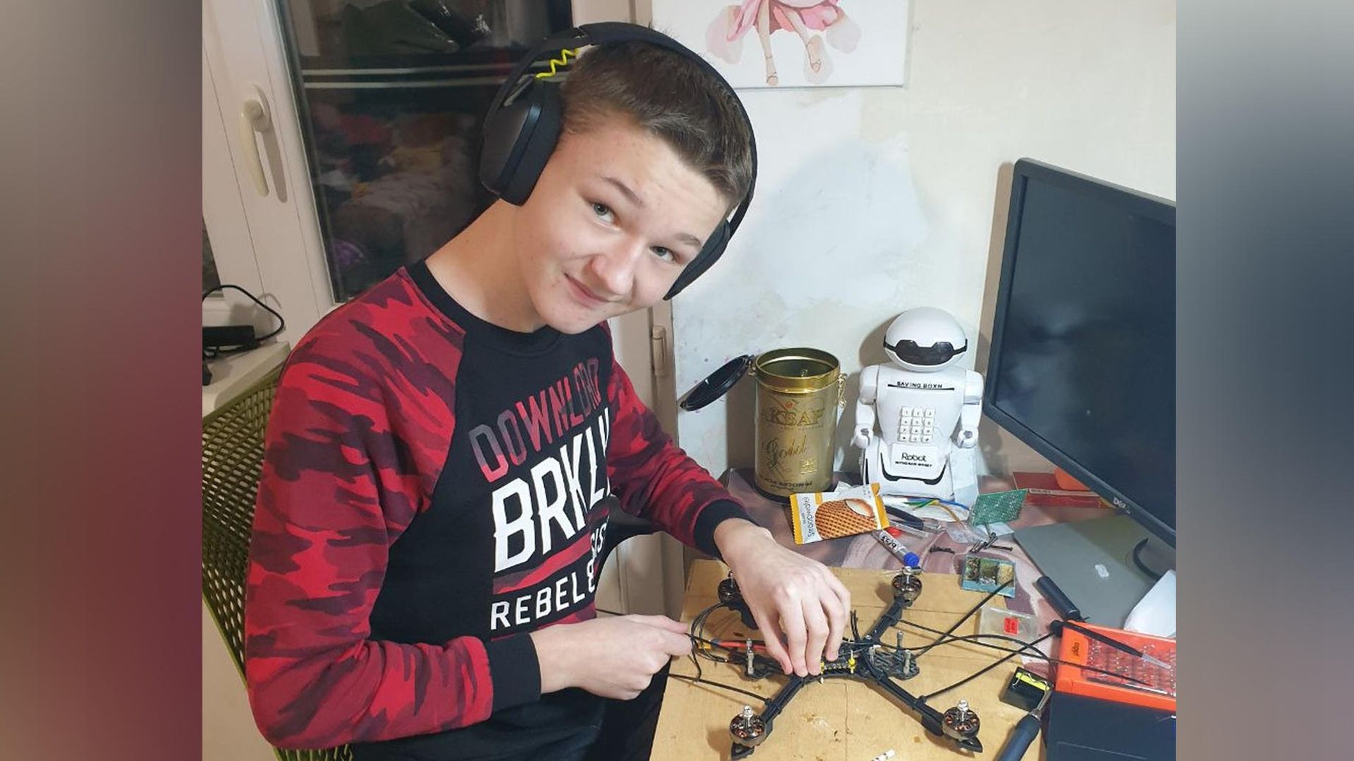 Підліток у навушниках сидить за письмовим столом і збирає дрон