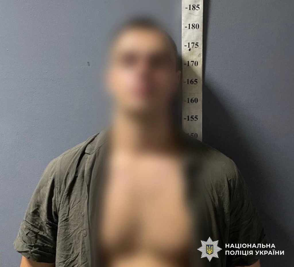 Чоловік в коричневій сорочці стоїть біля стіни в поліції із заблюреним обличчям