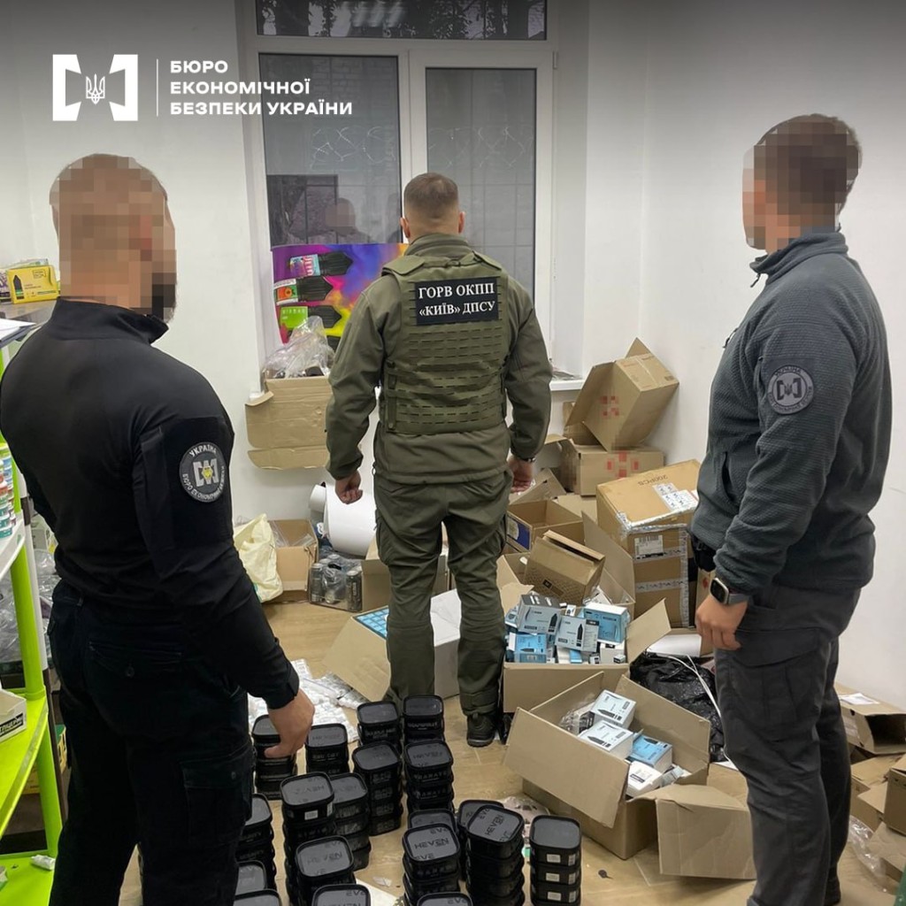Представники БЕБ і прикордонники стоять в приміщенні, де купа коробок із нелегальною продукцією