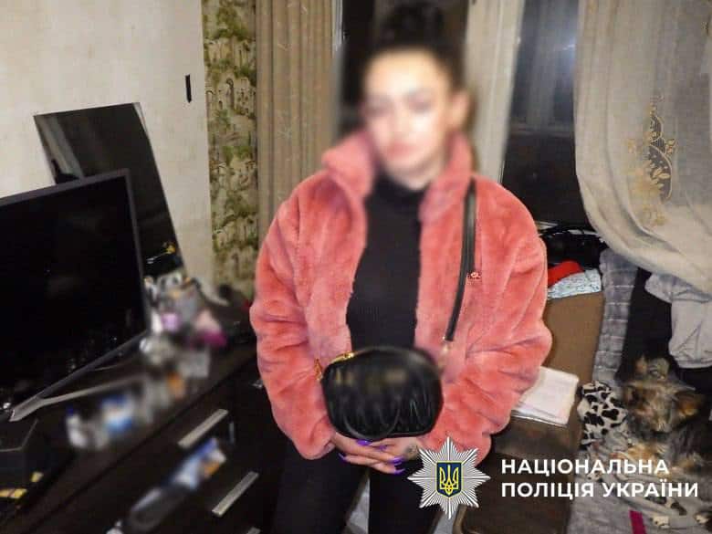 На Троєщині жінка відправляла метадон поштою у дитячих іграшках Підозрювана у збуті наркотиків стоїть в рожевій шубі і з чорною сумкою у кімнаті свого будинку із заблюреним обличчям