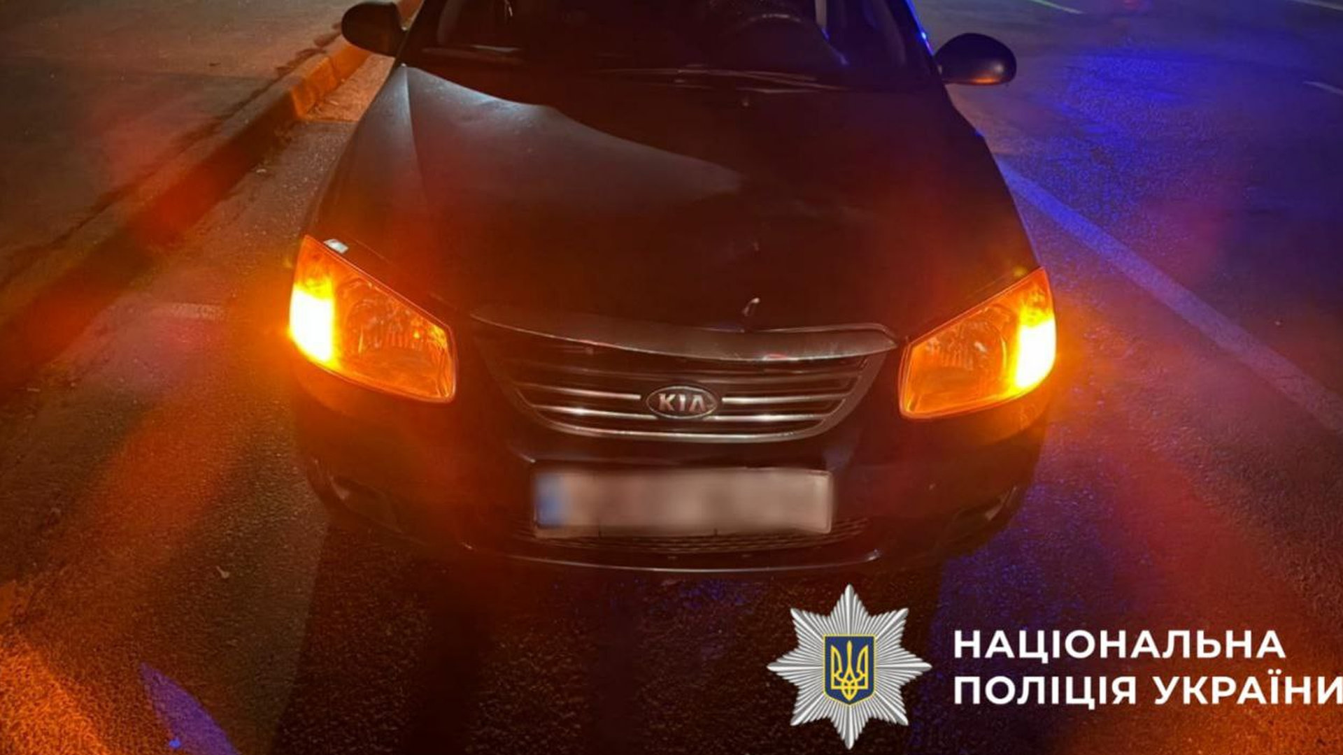 Автомобіль КІА із зімʼятим бампером стоїть вночі на дорозі із увімкненими фарами