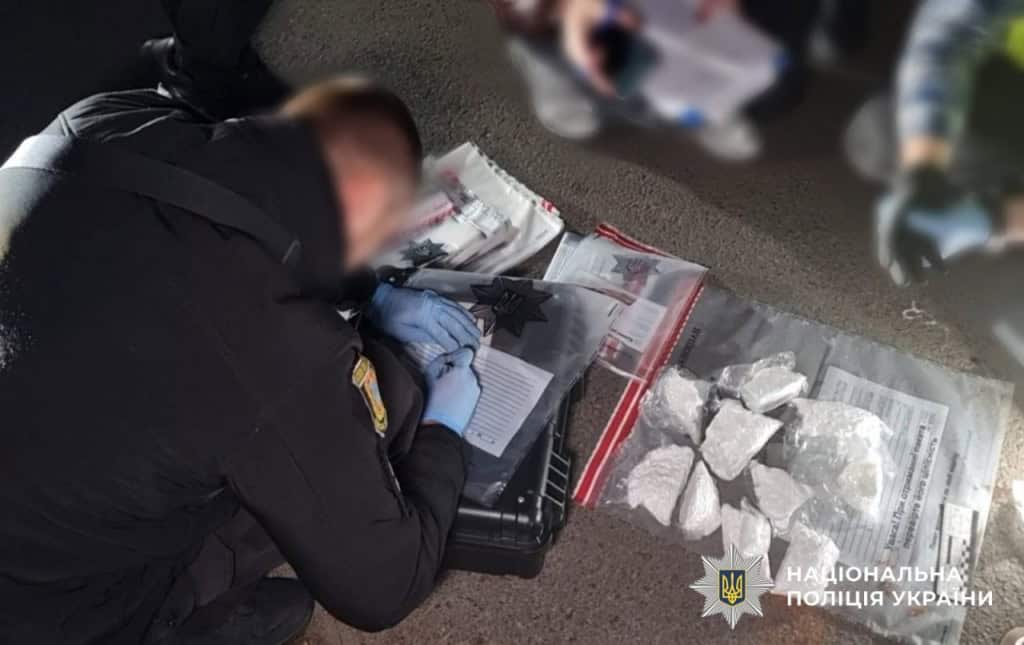 Правоохоронець працює з описанням речових доказів, він схилився над підлогою, на якій розклали кілька пакетів з наркотиками