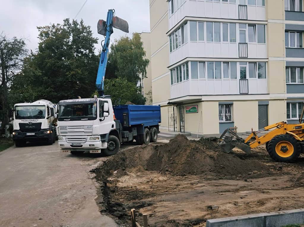Дві вантажівки працюють біля багатоповерхового будинку в Бучі, дороблюють газони і клумби