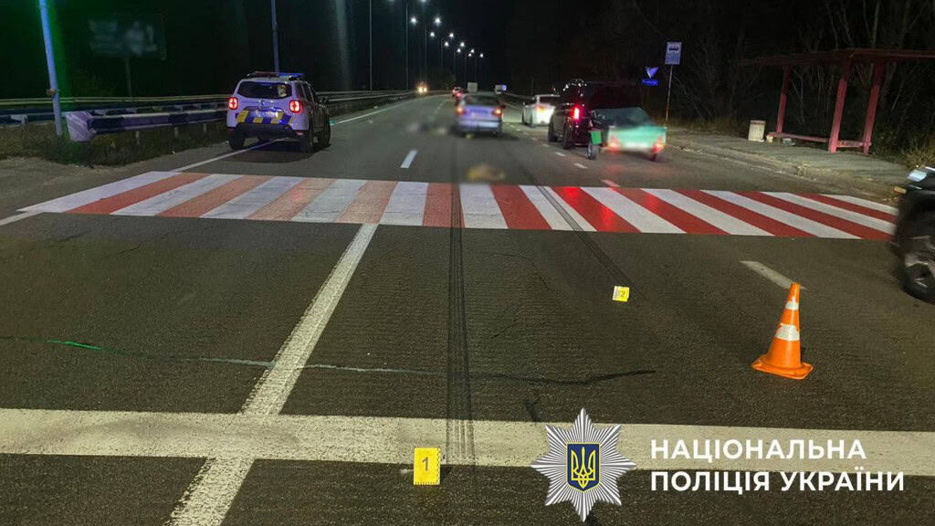 Пішохідний перехід у вигляді нерегульованої червоно-білої зебри на асфальті, поряд стоїть машина, яка збила людину