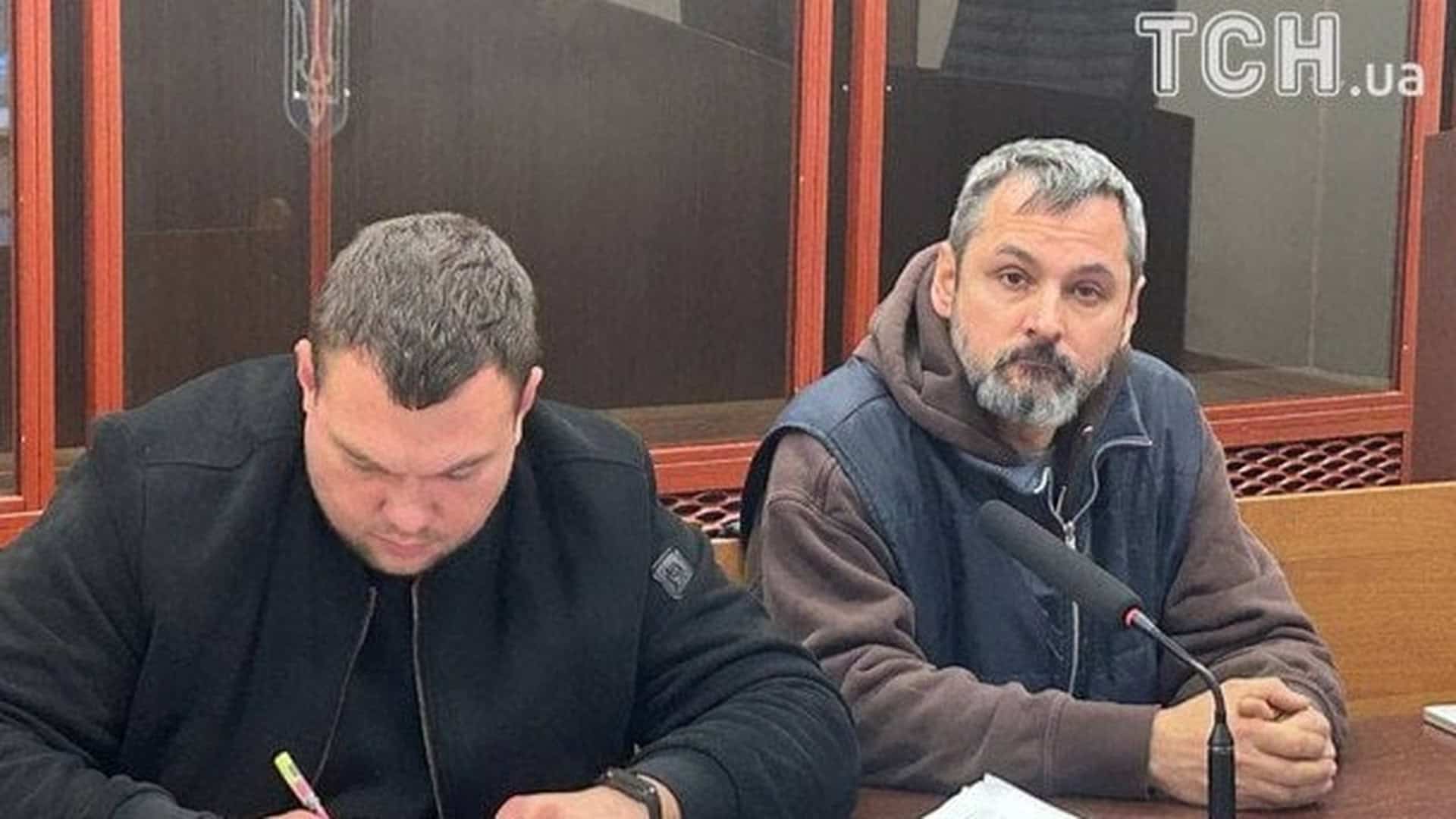 Двоє чоловіків у суді, один пише, інший сидить перед мікрофоном
