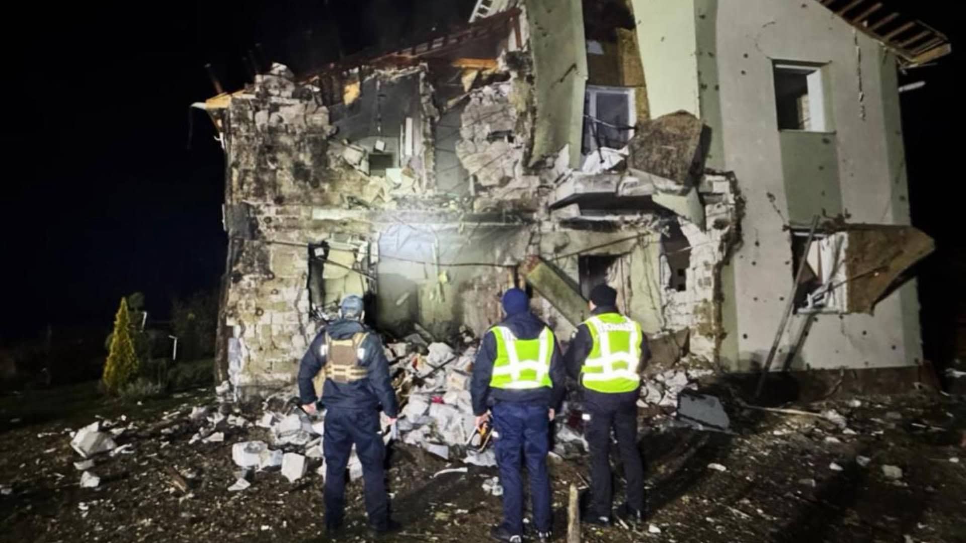 Зруйнований будинок в Київській області, троє поліцейських стоять і дивляться на нього в темноті
