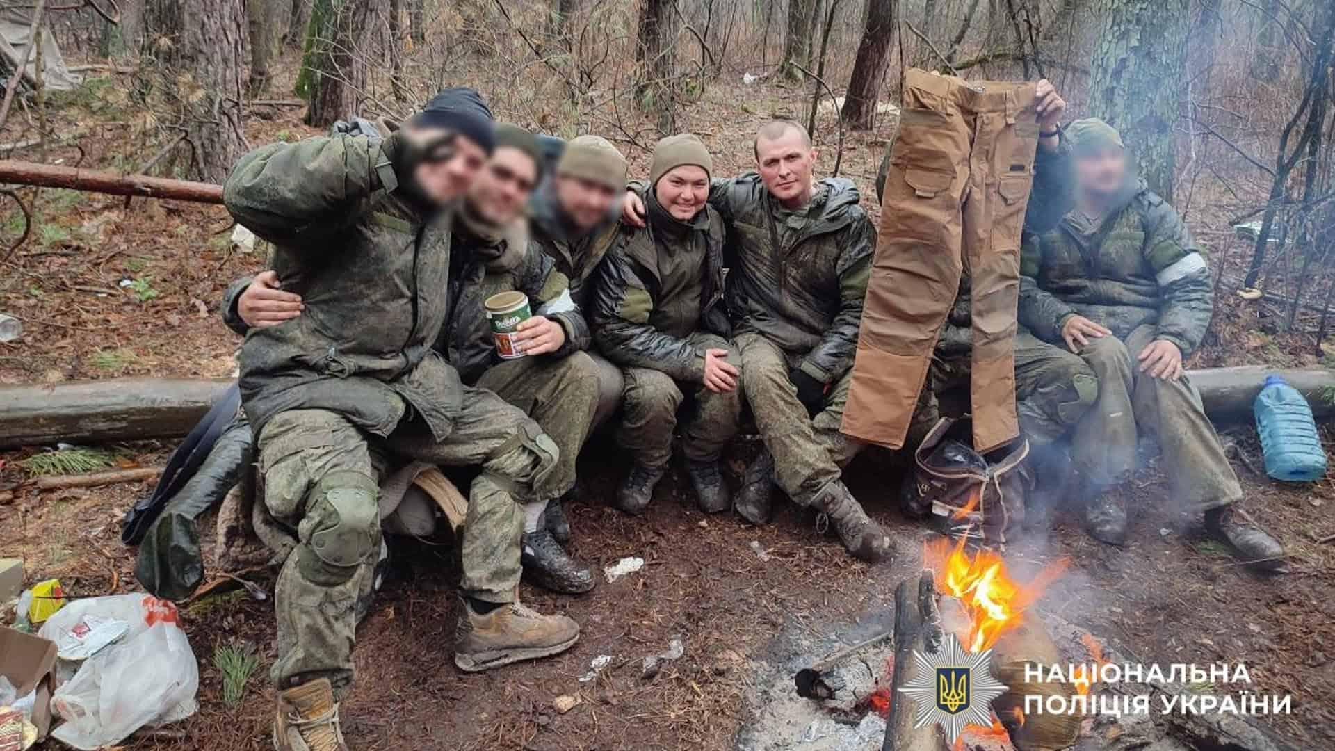 Російські солдати в камуфляжі сидять на колоді біля вогню в лісі