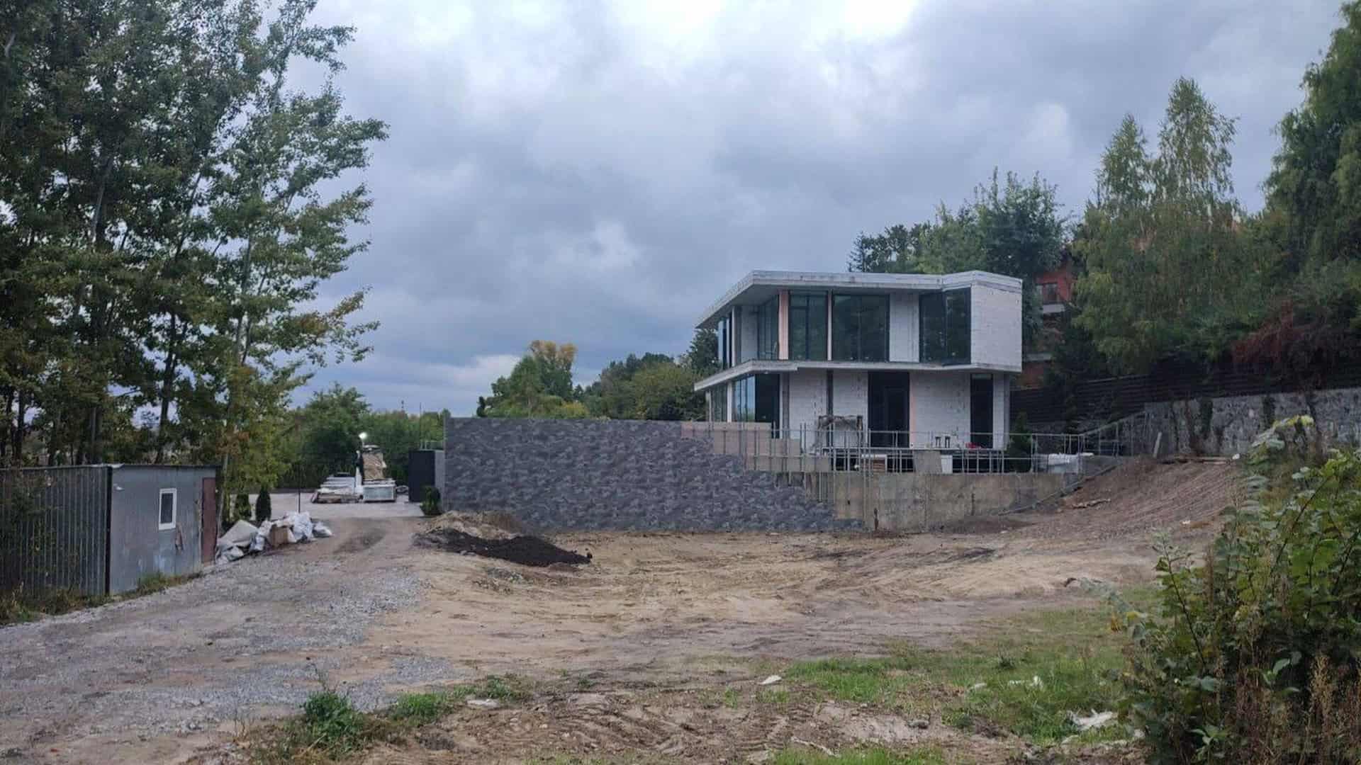Двоповерховий будинок на етапі будівництва біля природоохоронної зони, земляні роботи та будівельна техніка
