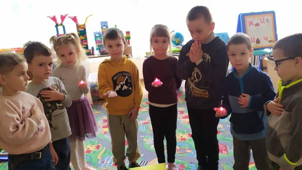 В дитсадку Києва показали як проводять хвилину мовчання Вісім дітей з дитячого садочку Києва стоять в приміщення групи дитсадка і вшановують памʼять загиблих воїнів. Троє з дітей тримають свічки в руках, хтось тримає руку біля серця