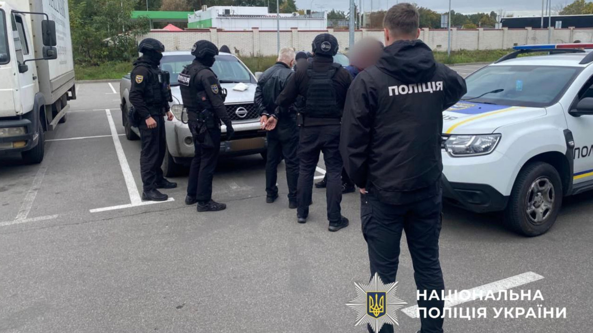 Команда правоохоронців проводить затримання підозрюваного на вулиці біля стоянки автомобілів