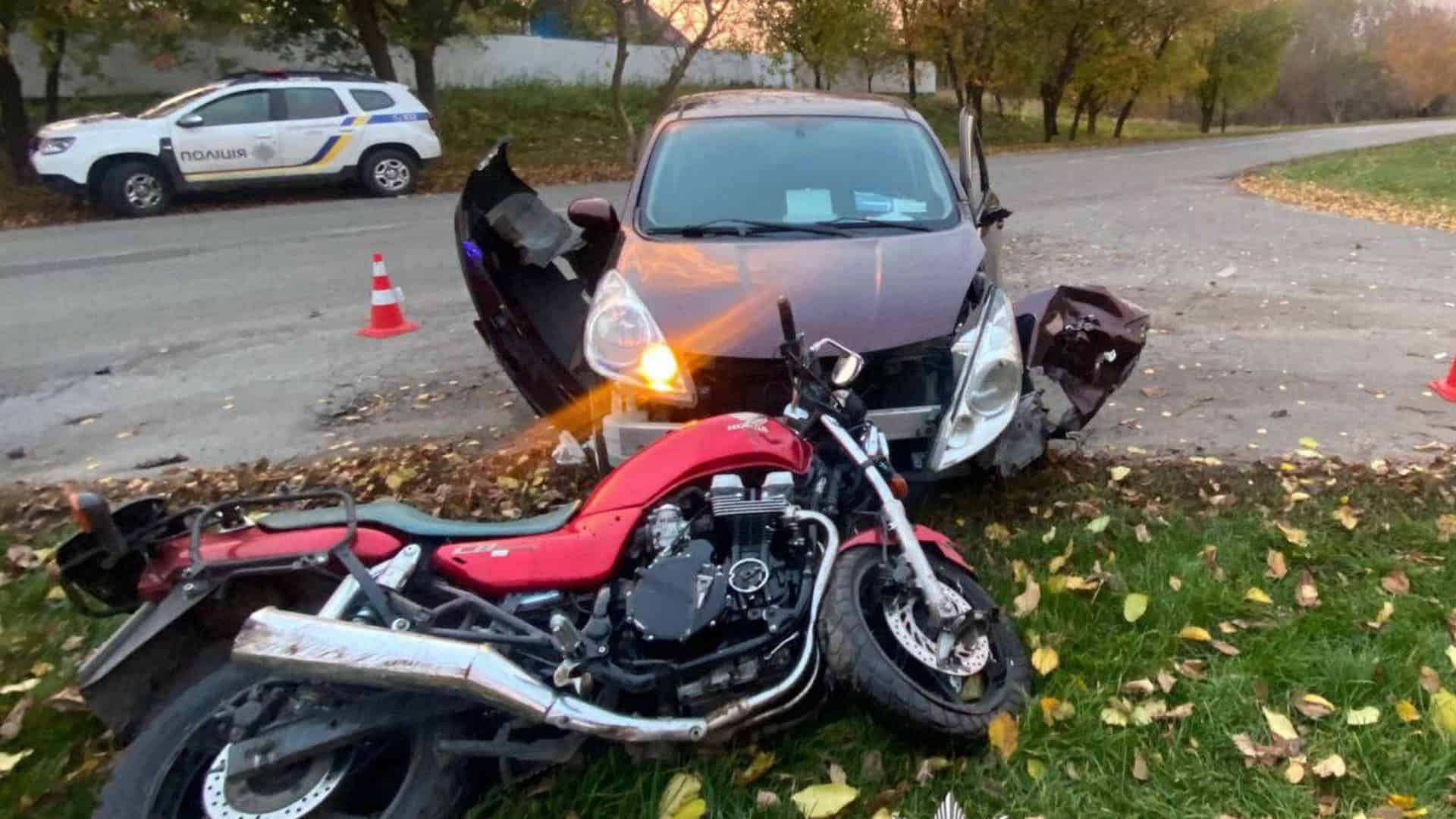 Червоний мотоцикл лежить на узбіччі поруч із легковим автомобілем, який має сильно пошкоджений перед