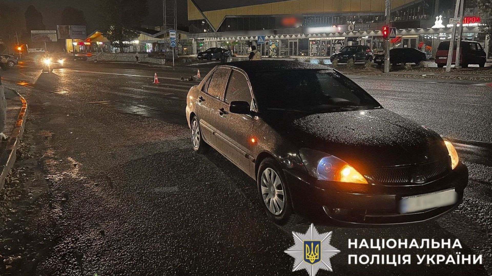 Чорний автомобіль стоїть на мокрій нічній дорозі з увімкненими фарами