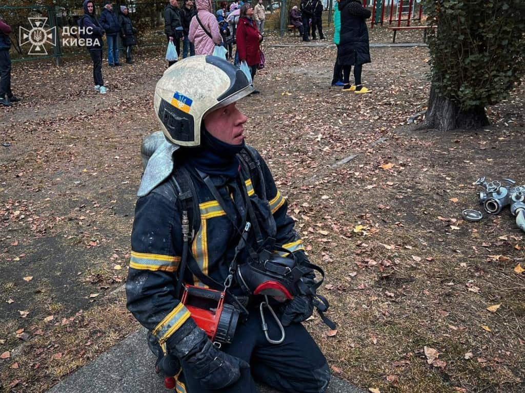Пожежа в багатоповерхівці на Лісовому проспекті: врятовано сімох людей, серед них троє дітей (фото) Пожежник у спорядженні відпочиває після гасіння пожежі, позаду видно мешканців будинку
