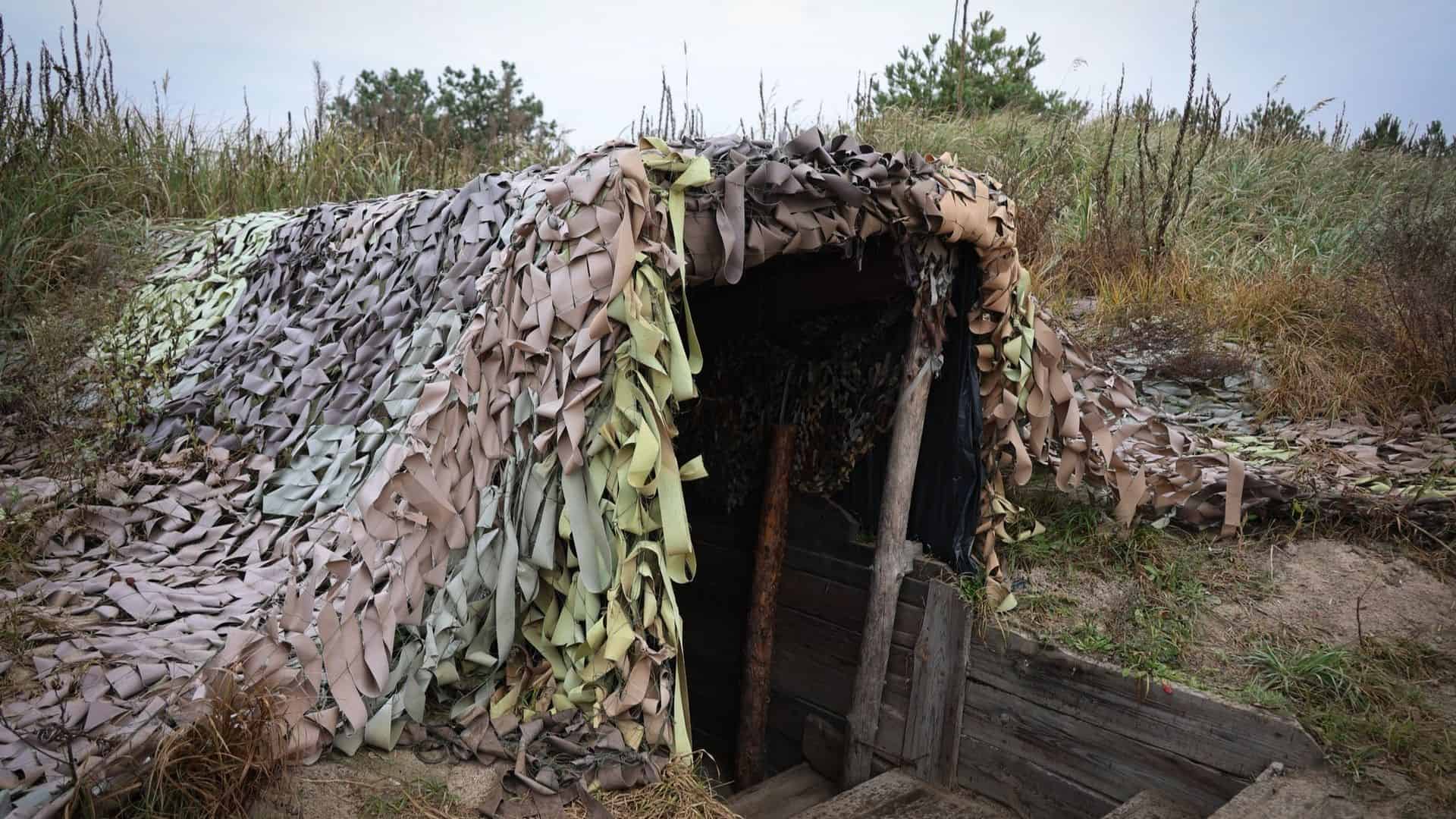Військовий бункер з камуфляжною сіткою, частково занурений у землю серед трави